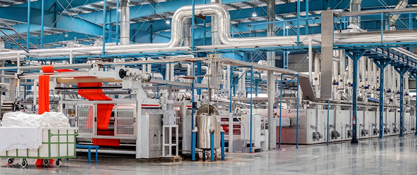 Interior of a large textile factory with industrial machines and rolls of red and white fabric.