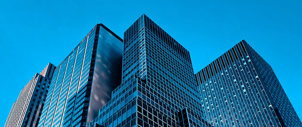 Low-angle view of modern glass skyscrapers against a clear blue sky.