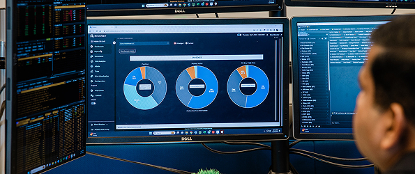 Person looking at three computer monitors displaying charts and data analytics dashboard.