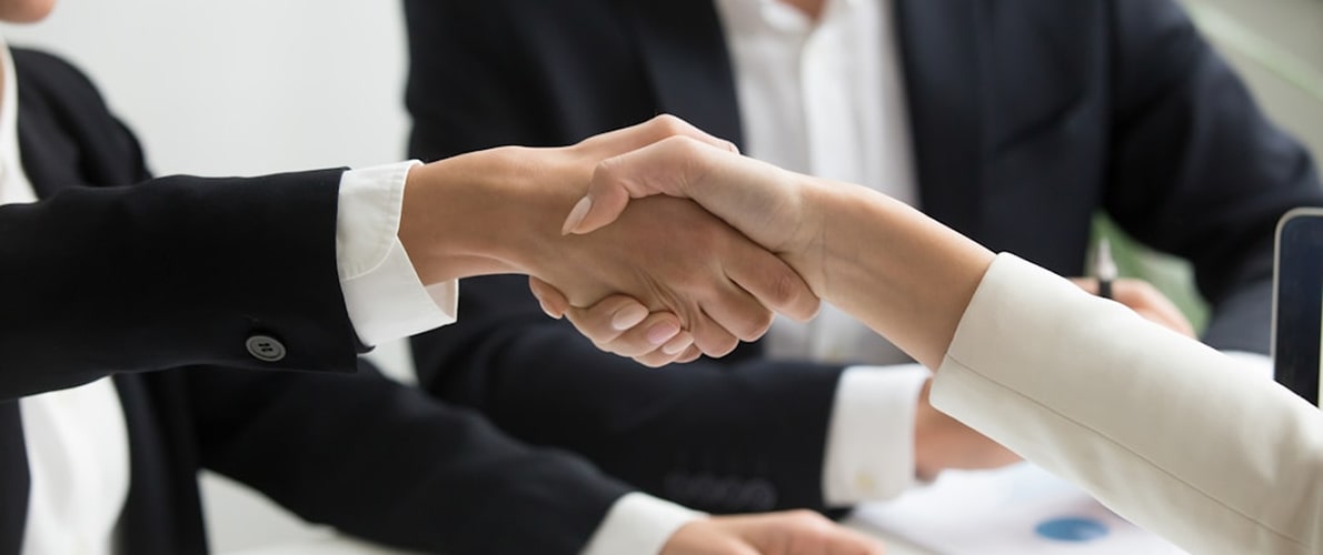 Two businesspeople shaking hands across a desk, symbolizing agreement or partnership.