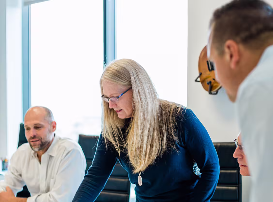 Three men and one woman in a meeting with a guitar hanging on the wall by the window.
