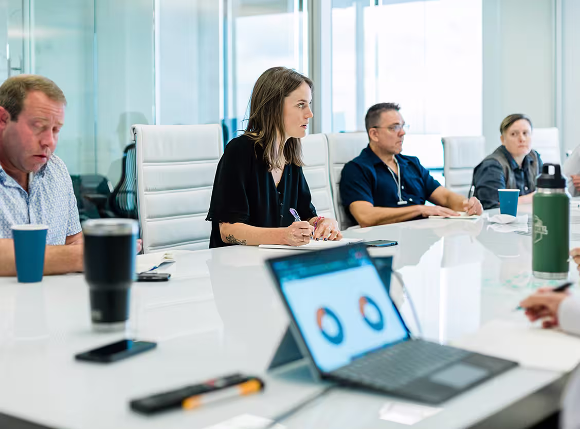 People in a modern office meeting room with a laptop showing charts on a glossy table.