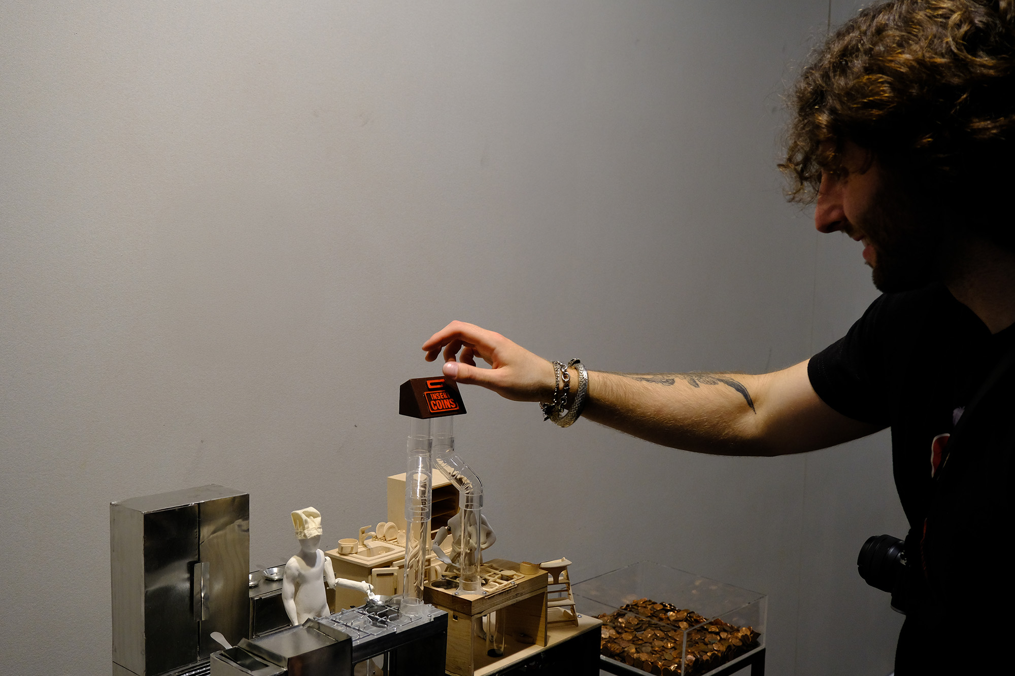 Photograph of the project at my thesis show, with a person just about to drop a penny into the slot. 