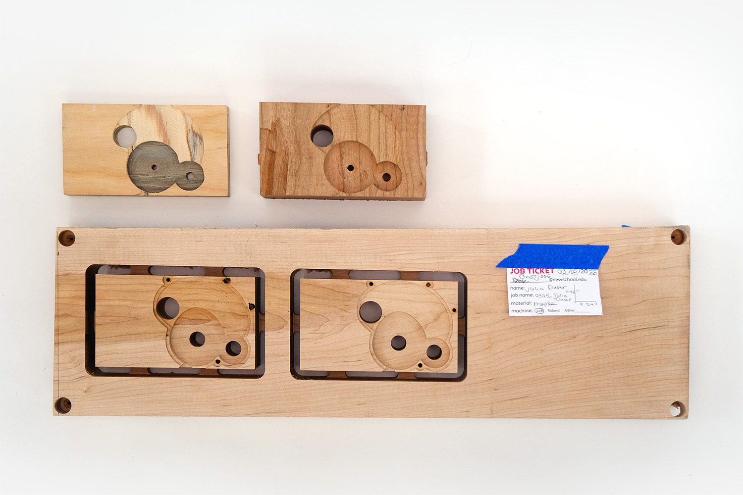 Photograph of three wood pieces that have been CNC cut to hold gears. 