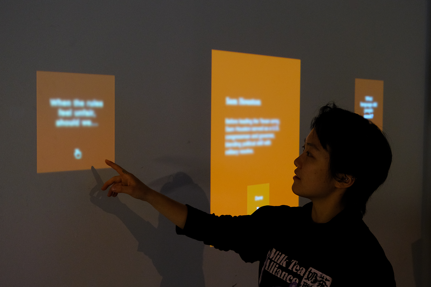 Person pointing at three orange digital screens projected on a wall with blurred text.