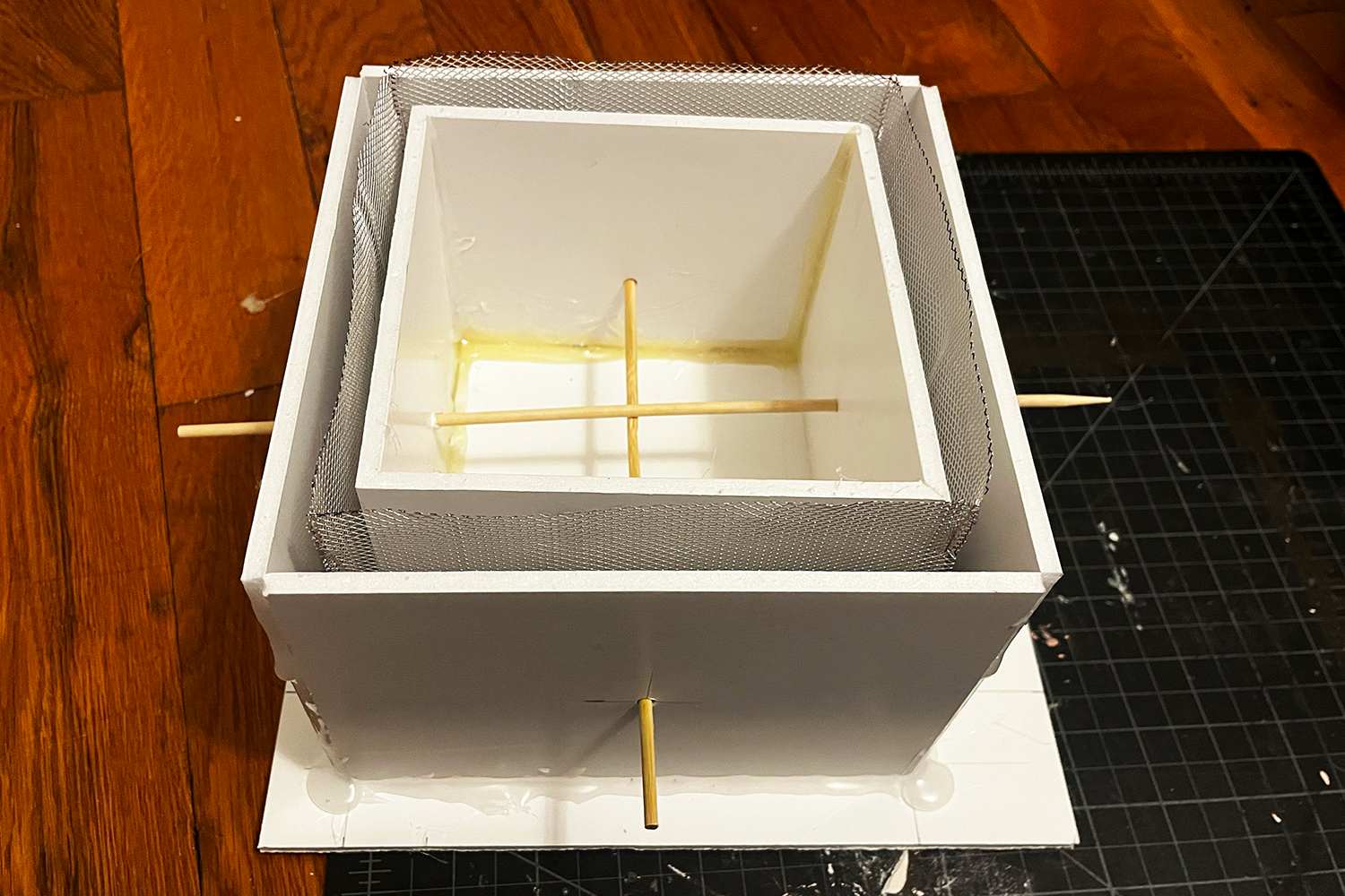 White layered square foam structure with mesh sides and wooden sticks crossing inside and extending through the sides.
