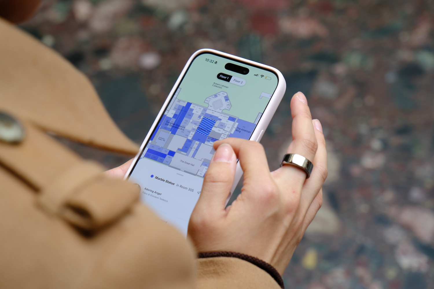 Person holding a smartphone displaying a museum floor map with marked rooms and artwork details.