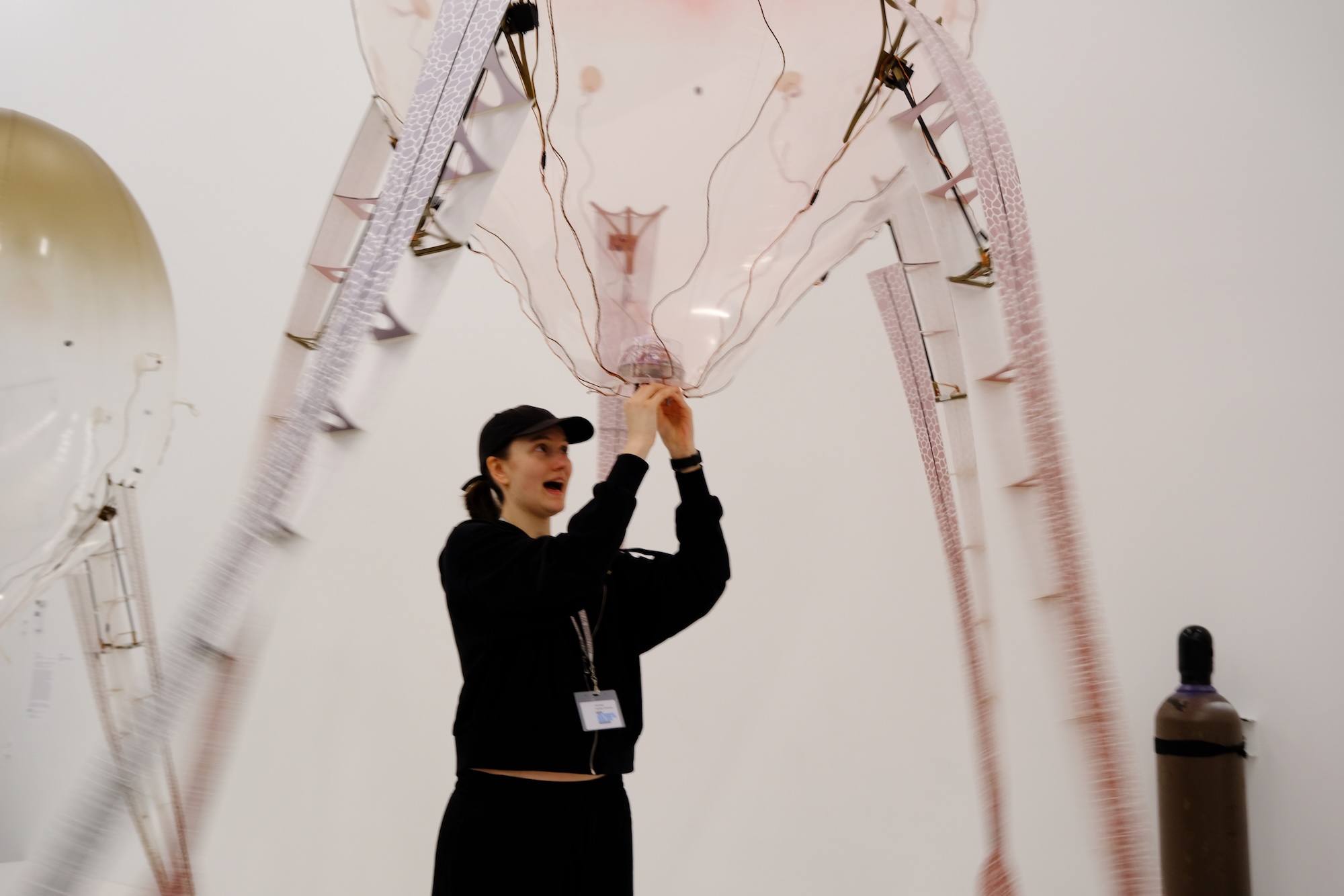 Person holding a translucent art installation with wires at a gallery.
