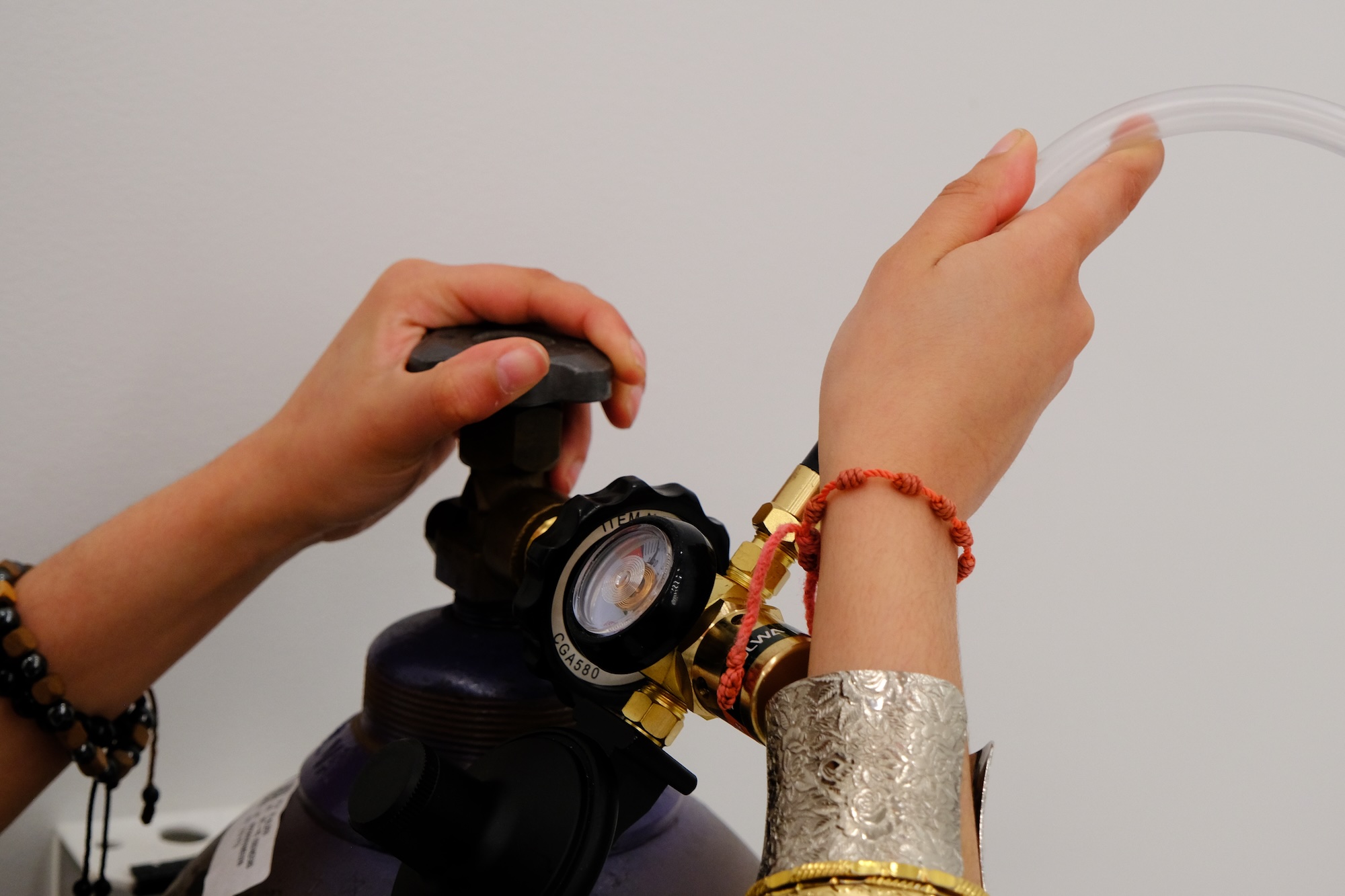 Two hands adjusting a valve on a gas cylinder connected to a clear plastic tube.