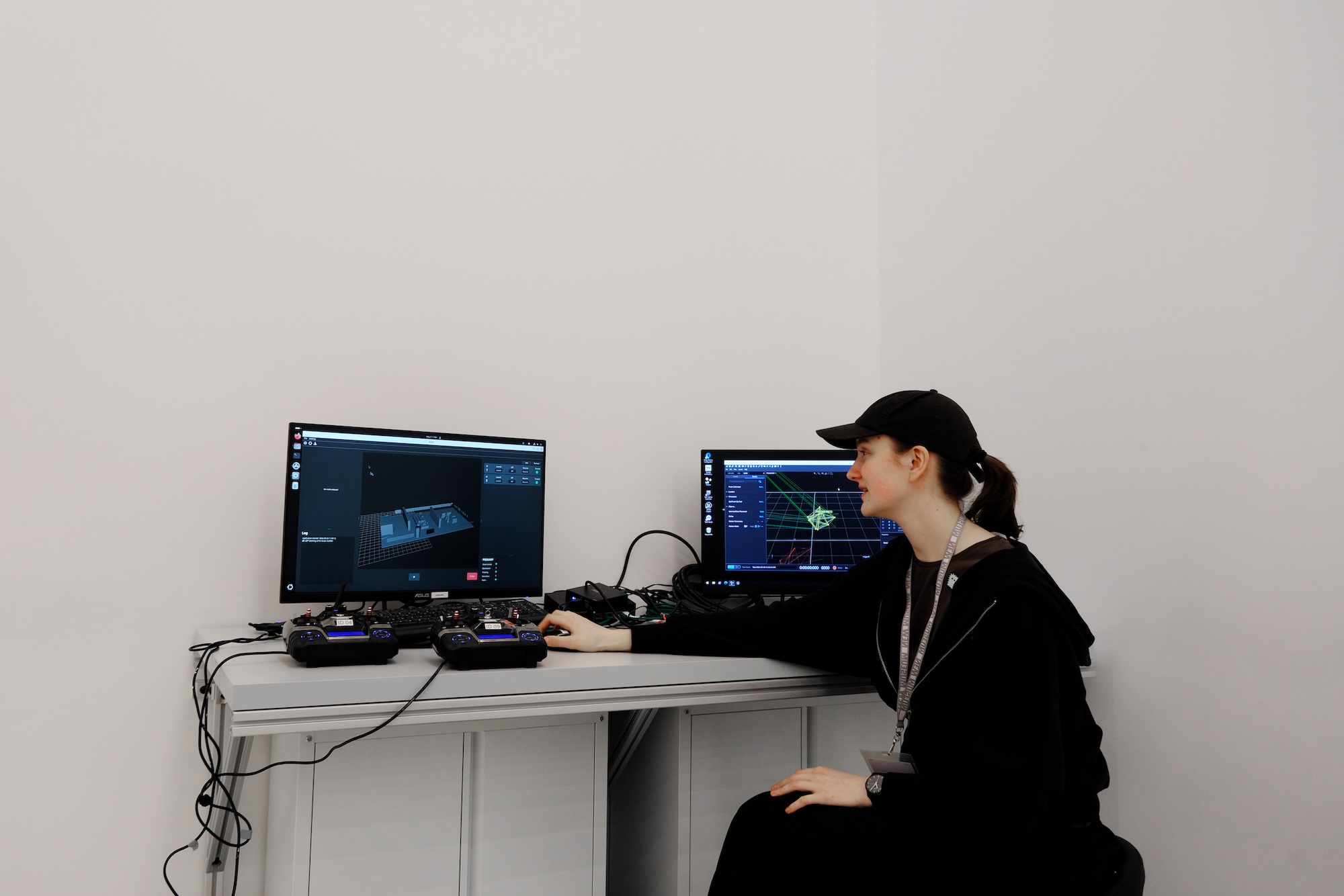 Person wearing black cap sitting at desk with two monitors showing 3D modeling software.