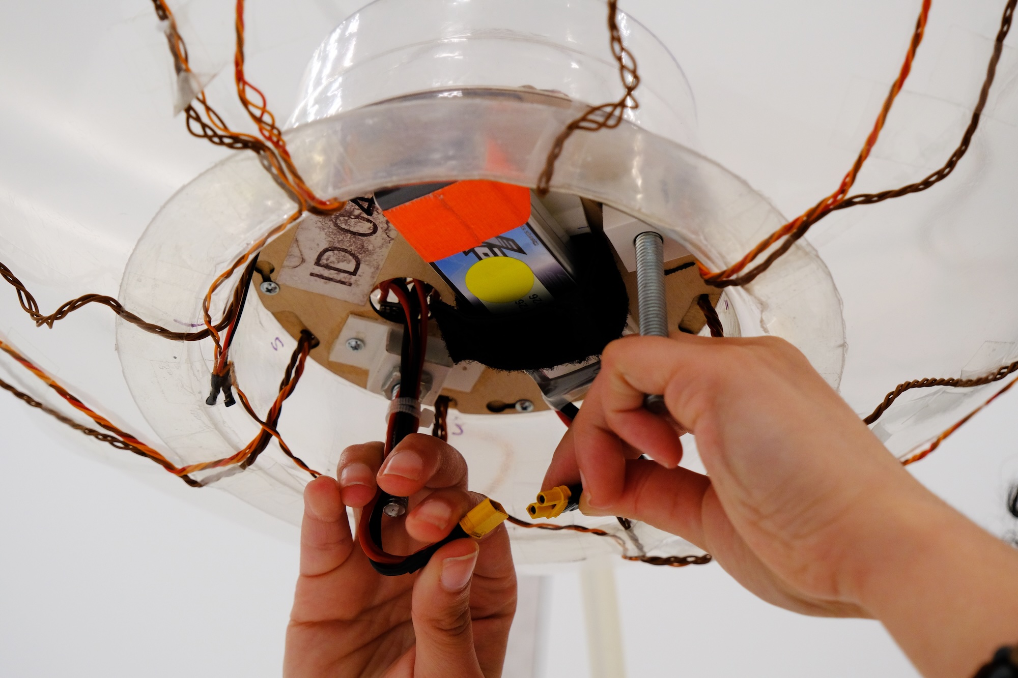 Hands connecting yellow electrical connectors inside a device with visible wires and a battery.
