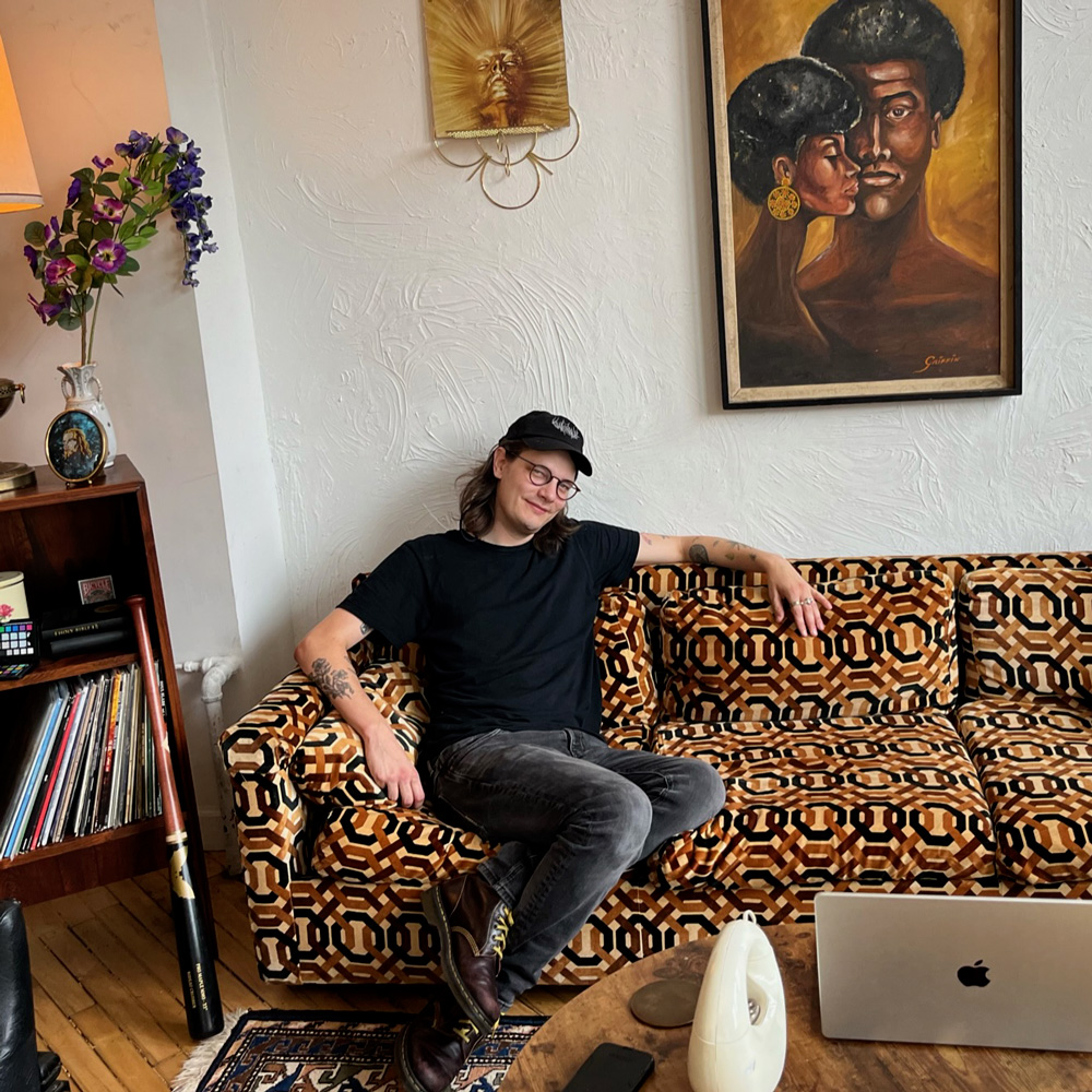 Jordan Rundle sitting on a mid-century couch, smiling and looking at the camera.