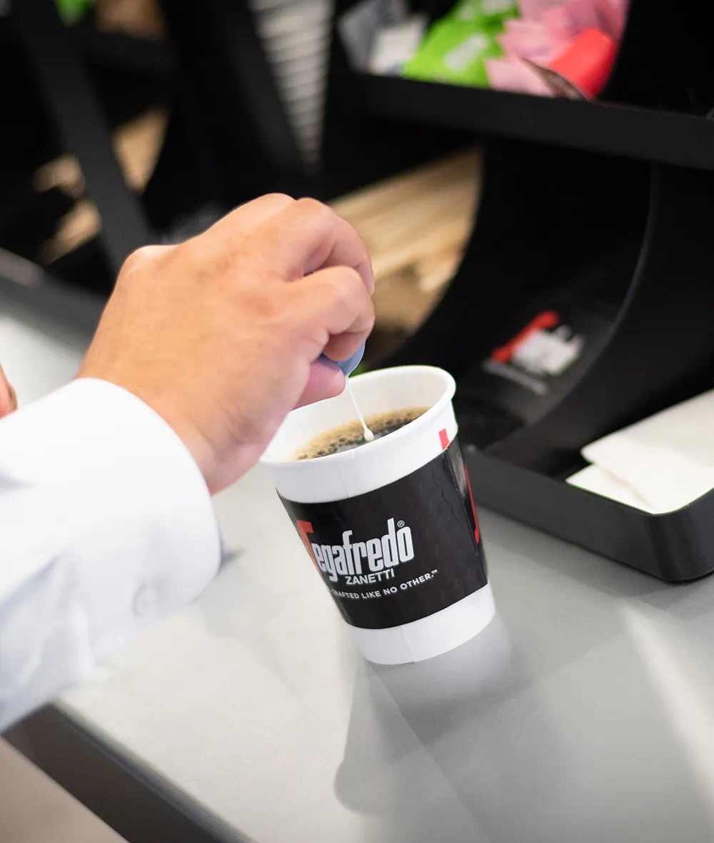 Hand stirring a hot coffee in a white and black Segafredo Zanetti branded cup on a counter.