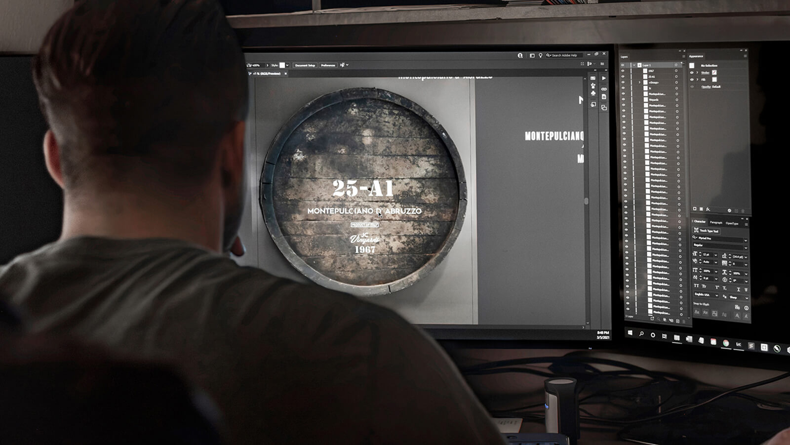 Designer at Cegrix working on a wine barrel branding project in Adobe Photoshop, shown on dual monitors.
