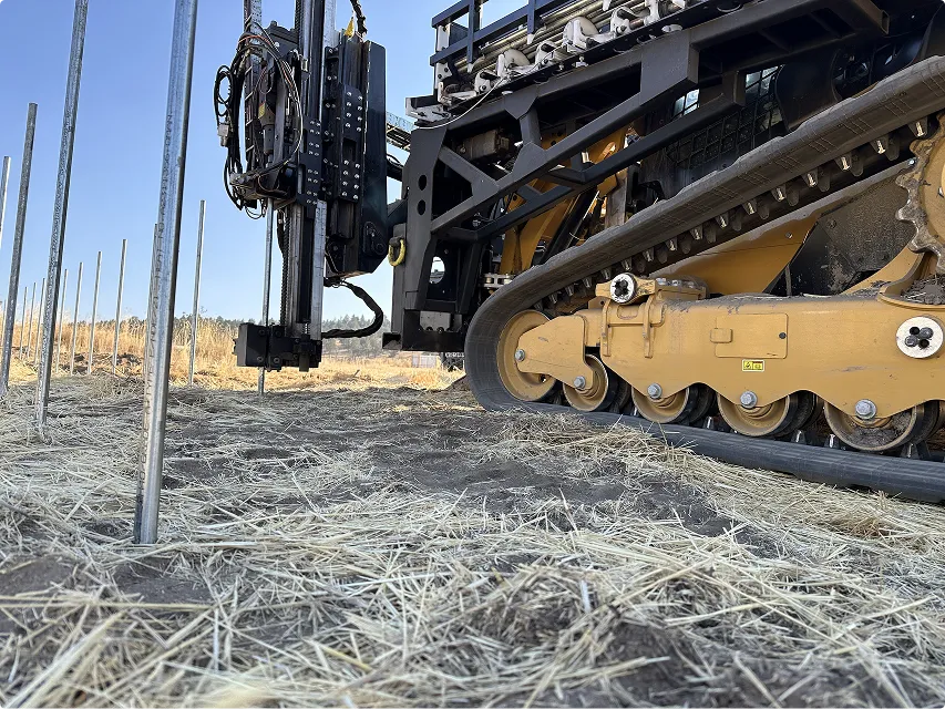 Solar pile driver installing metal posts in a field.