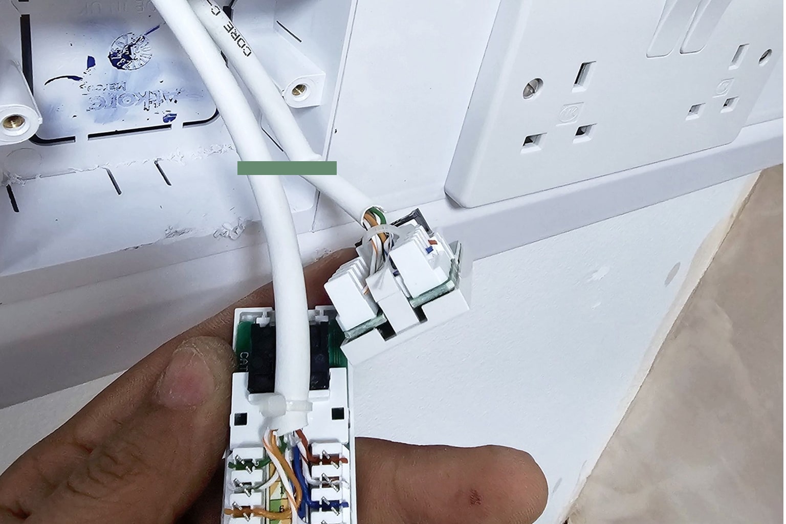 Close-up of a hand holding a white Ethernet cable connected to a network socket near wall power outlets.