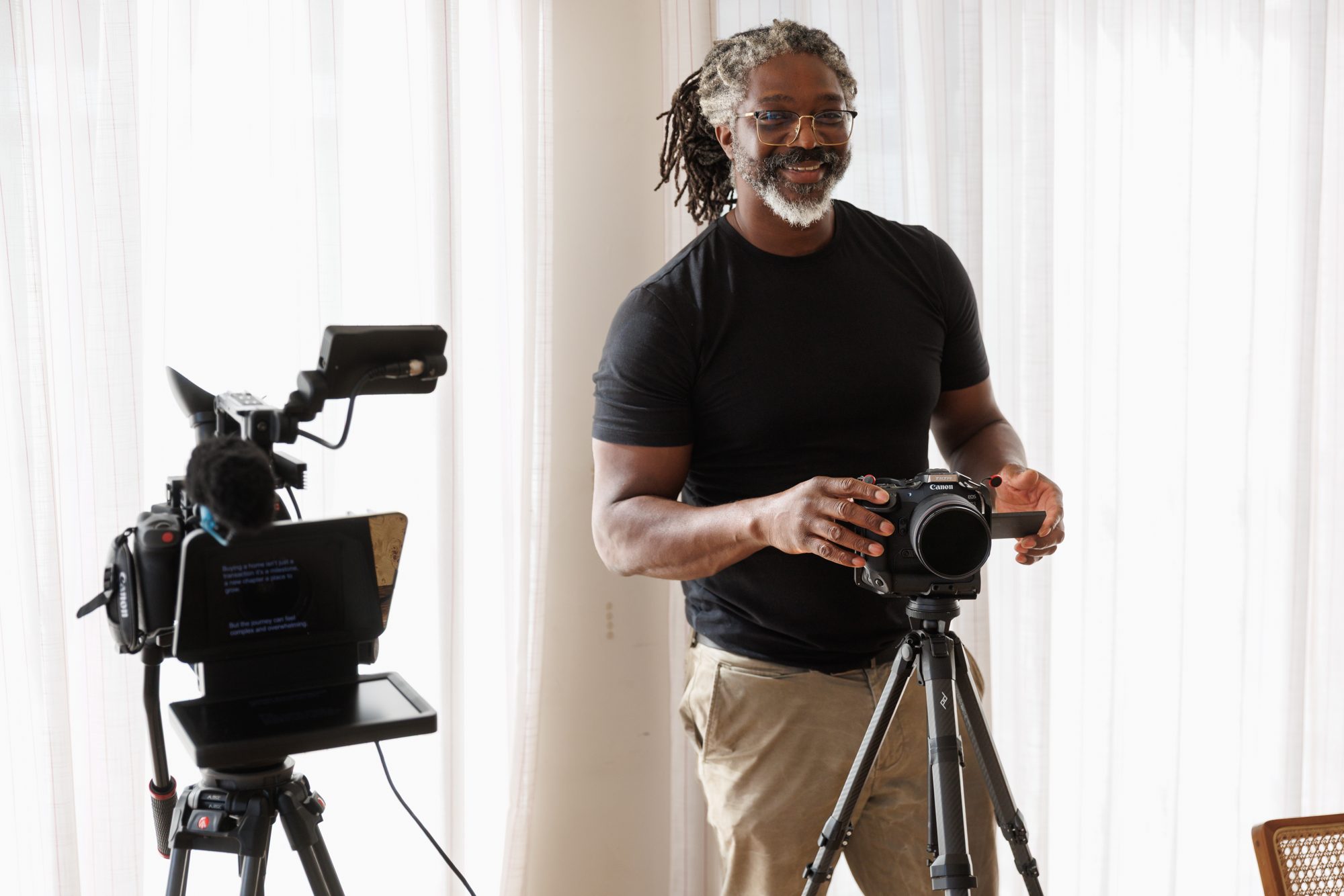 Kevan Smith smiling at the lens with his hands on a camera, a teleprompter rig beside him