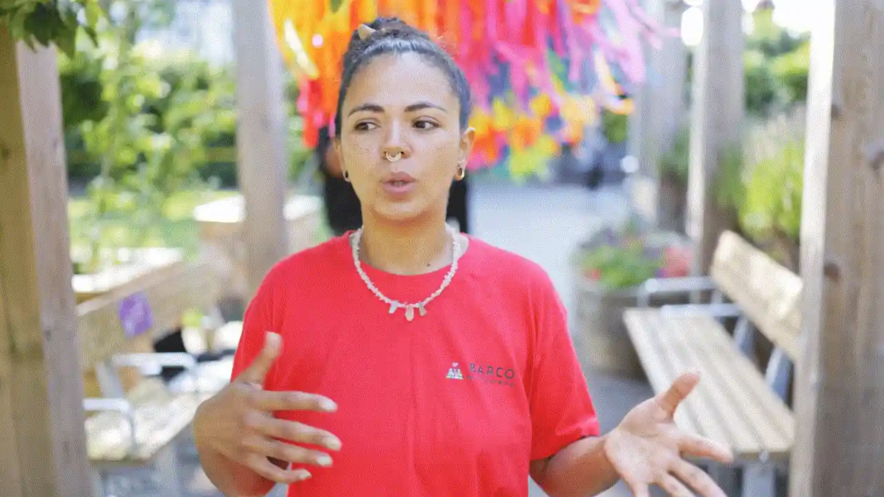 A woman in a red top speaking outdoors under colourful bunting.