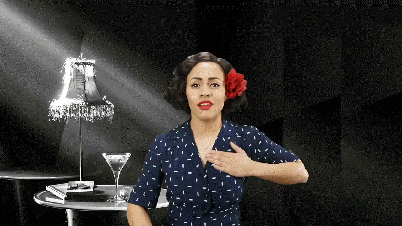 A performer in a polka-dot dress, hand on her heart, beside a lamp in a dark bar.