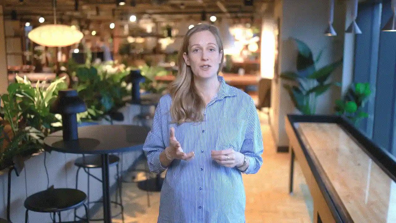 A facilitator speaking to camera in a café workspace.