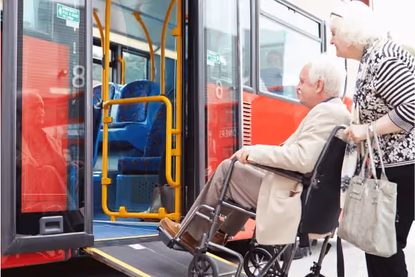 Photo of a man in a wheelchair being pushed up a ramp to get on a bus.