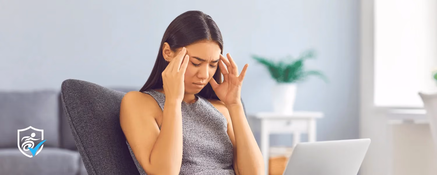 Photo of a woman sitting down with her laptop on her lap and fingers on her temples