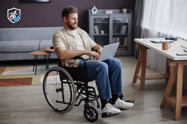 Man in a wheelchair with a laptop on his lap in a sitting room: how to register as disabled UK