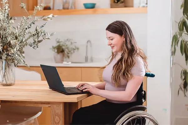 photo of a woman in a wheelchair sitting at a desk using a laptop