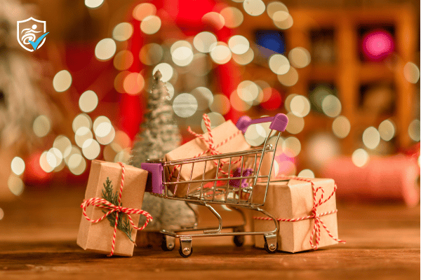 Photo of wrapped christmas gifts next to a mini shopping trolley in front of blurred glowing lights