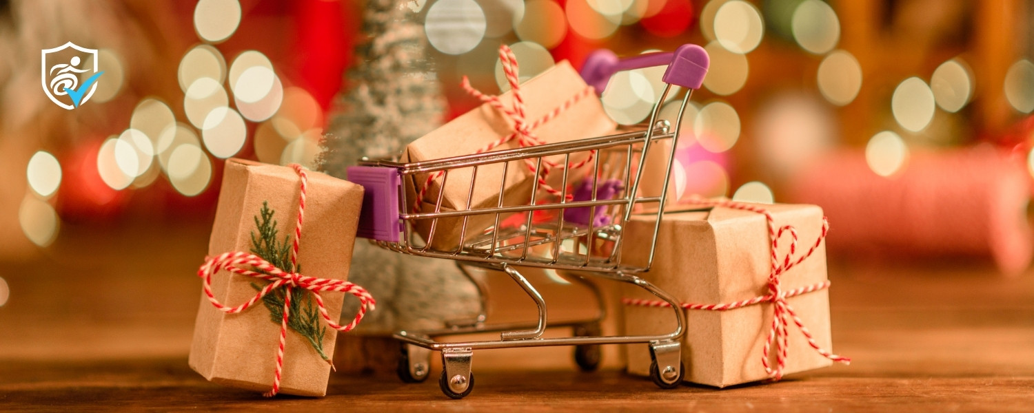 Photo of wrapped christmas gifts next to a mini shopping trolley in front of blurred glowing lights