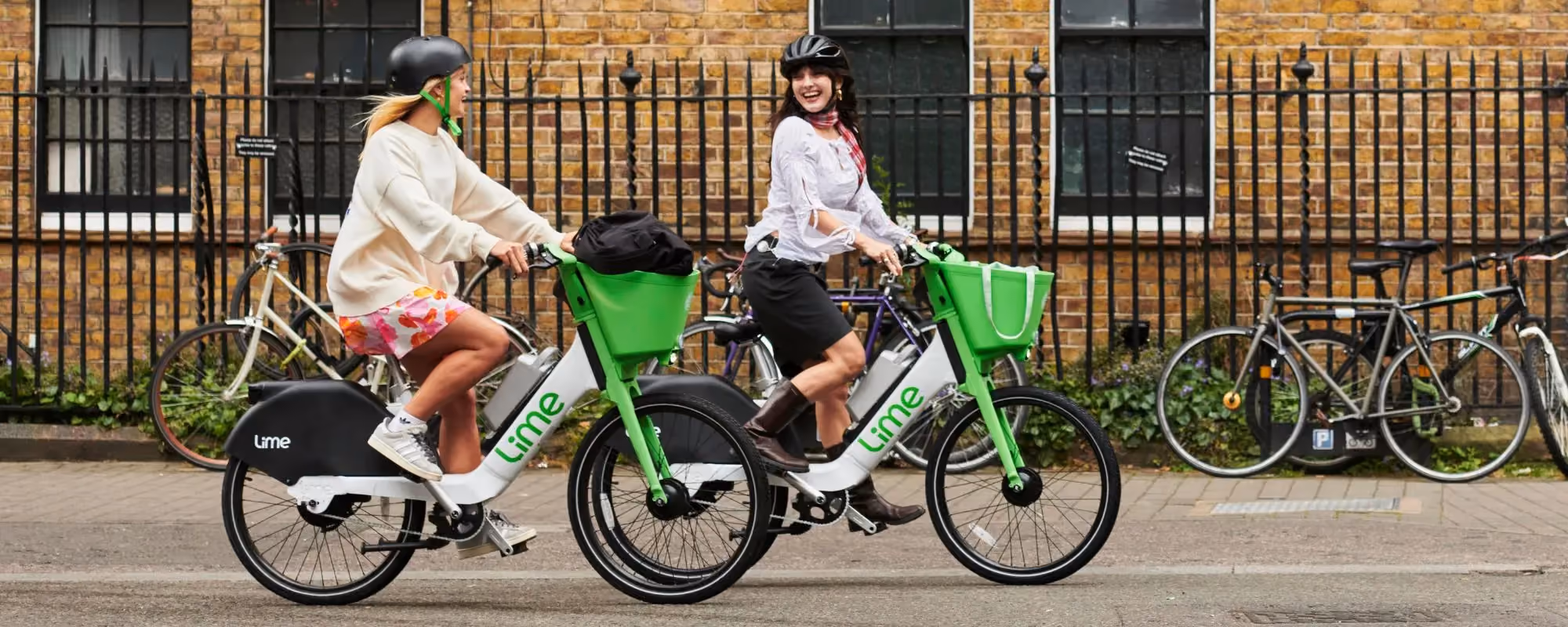 Two women riding Lime bicycles through a city street.