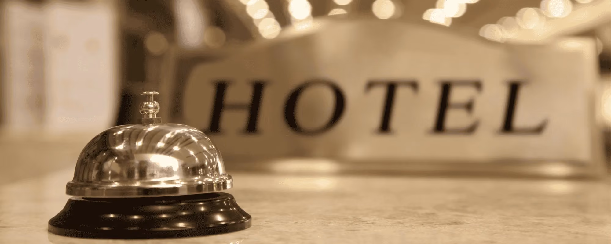 Hotel reception bell on a front desk with blurred hotel sign in background.