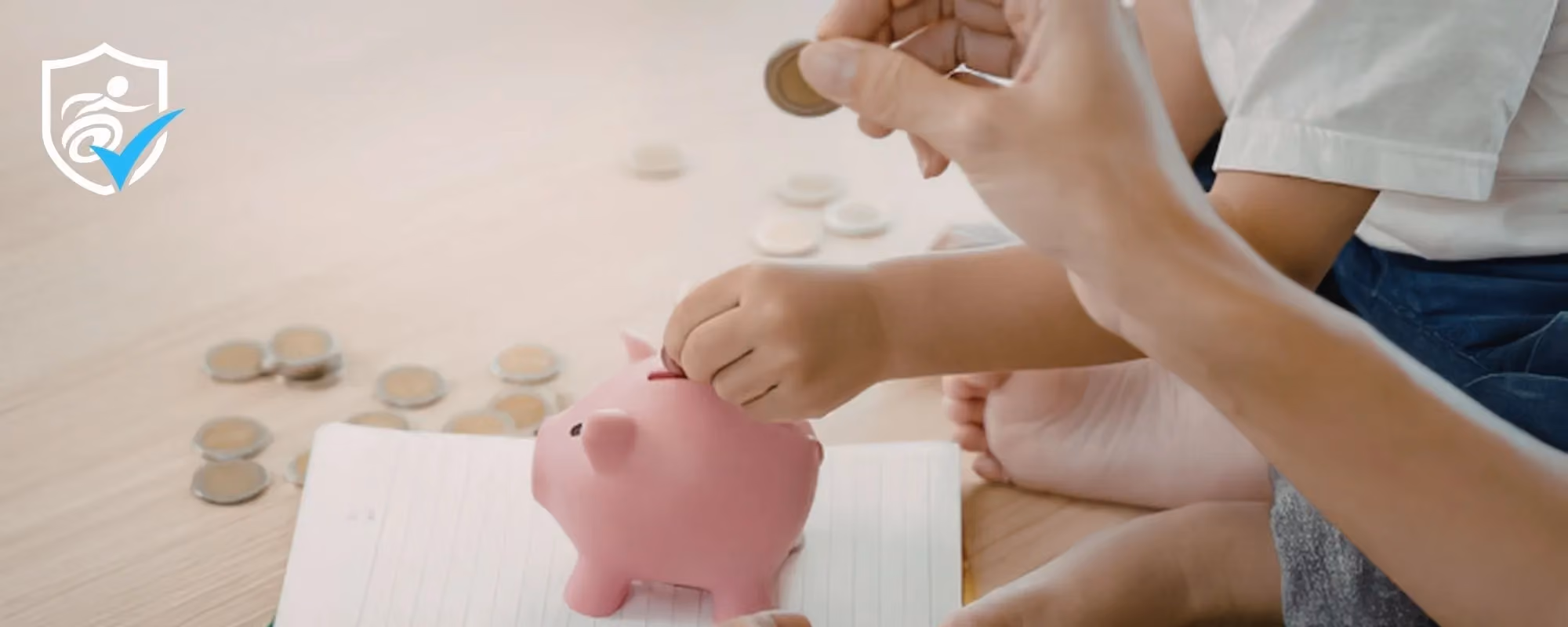 A photo of two hands holding a coin ready to drop it into a piggy bank.