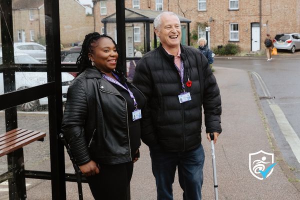 Thumbnail photo of a man and woman wearing National Disability Cards standing under a bus stop