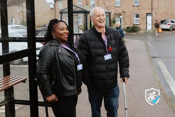 Thumbnail photo of a man and woman wearing National Disability Cards standing under a bus stop