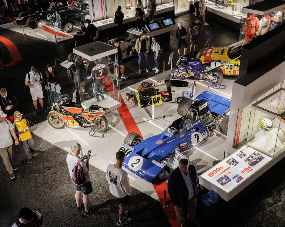 People standing around a display at Silverstone Museum showcasing a race car and three motorbikes