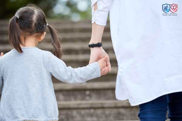 A woman and a little girl are walking and holding hands.