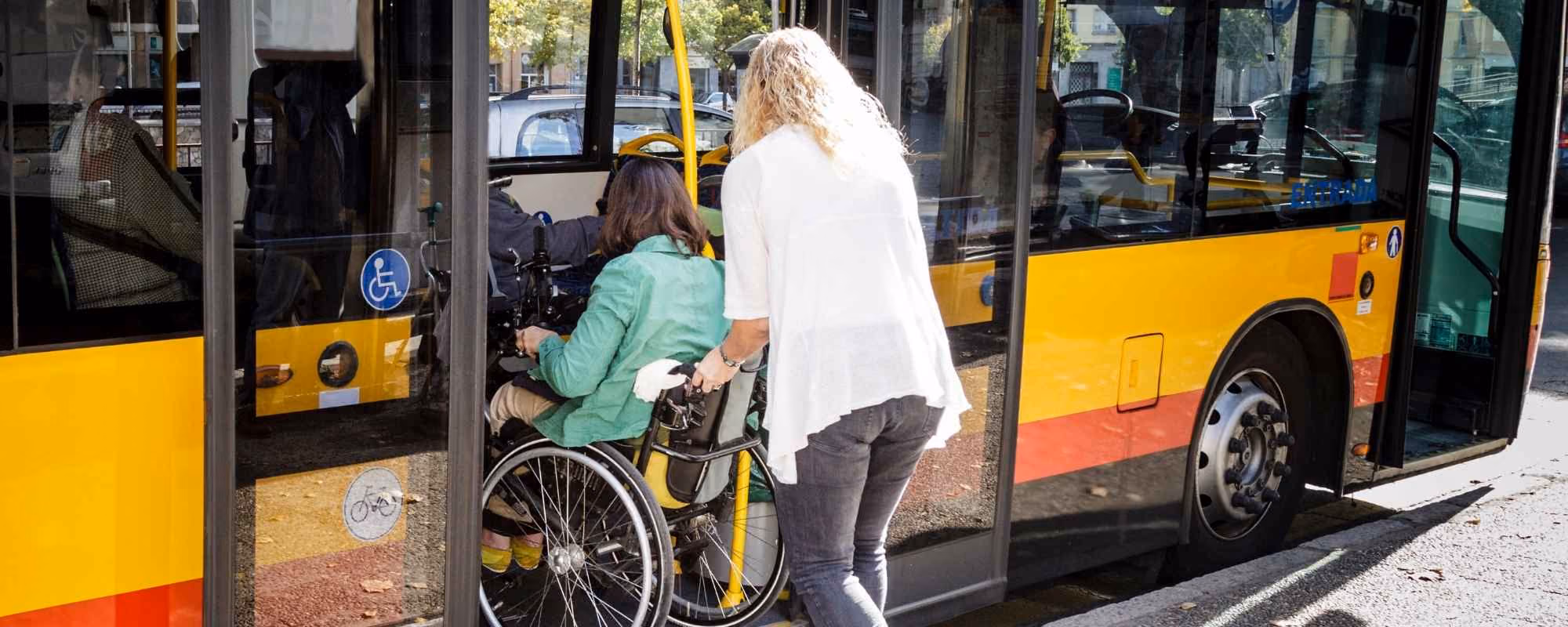 A blond woman helping a woman in a wheelchair get onto a yellow bus