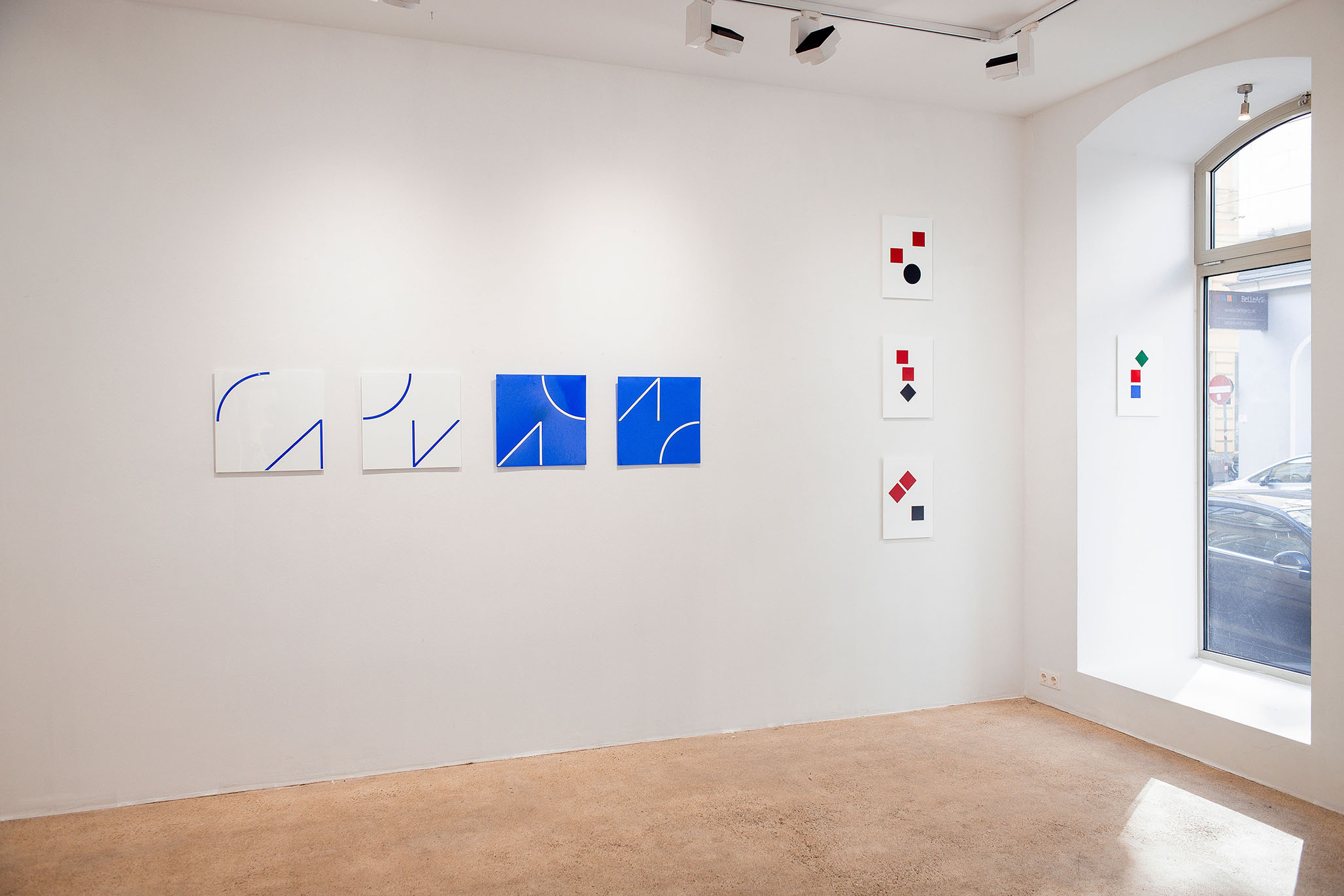 Exhibition view of Fritz Pechmann’s acrylic concrete artworks in Vienna, 2025. A series of white and blue square panels with precise curved line compositions is showcased alongside vertical white panels with bold red, black, and green geometric shapes. These minimalist acrylic concrete pieces capture the artist’s signature balance of structure, color, and materiality, presented in a bright, contemporary gallery with natural light.

