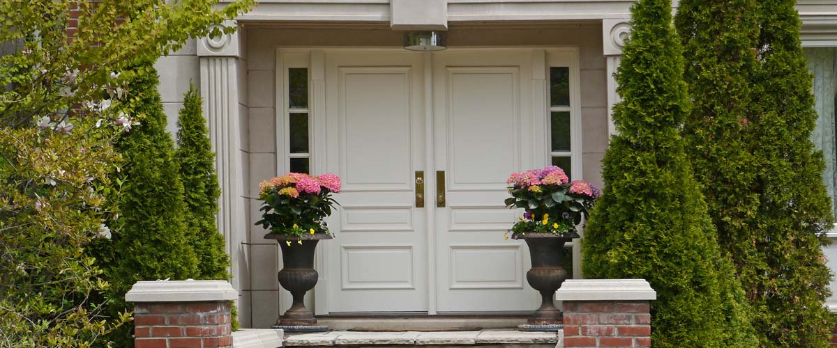 White double front entry doors with decorative plants and brick columns