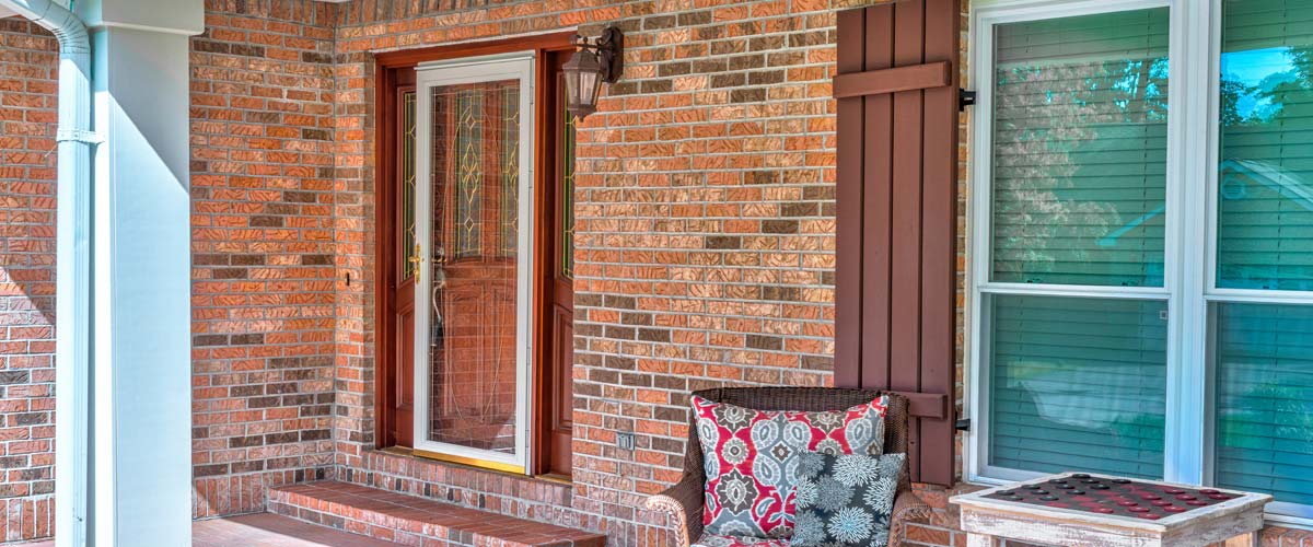 Brick house with a glass storm door and a porch seating area.