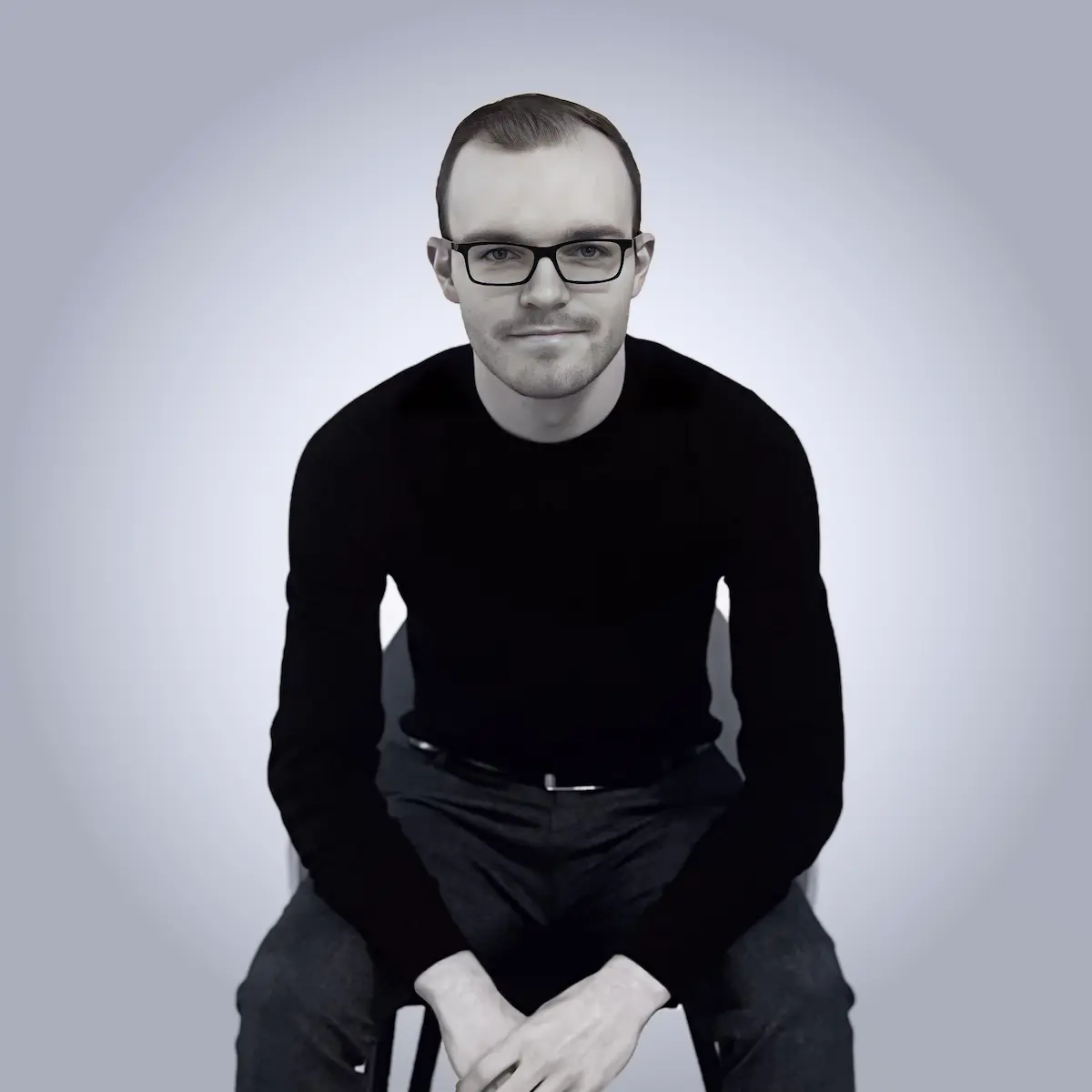 Greyscale image of Jan facing the viewer while sitting in a chair, slightly leaning front
