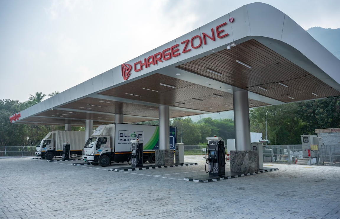 Two electric logistics trucks charging at a covered, multi-bay ChargeZone station