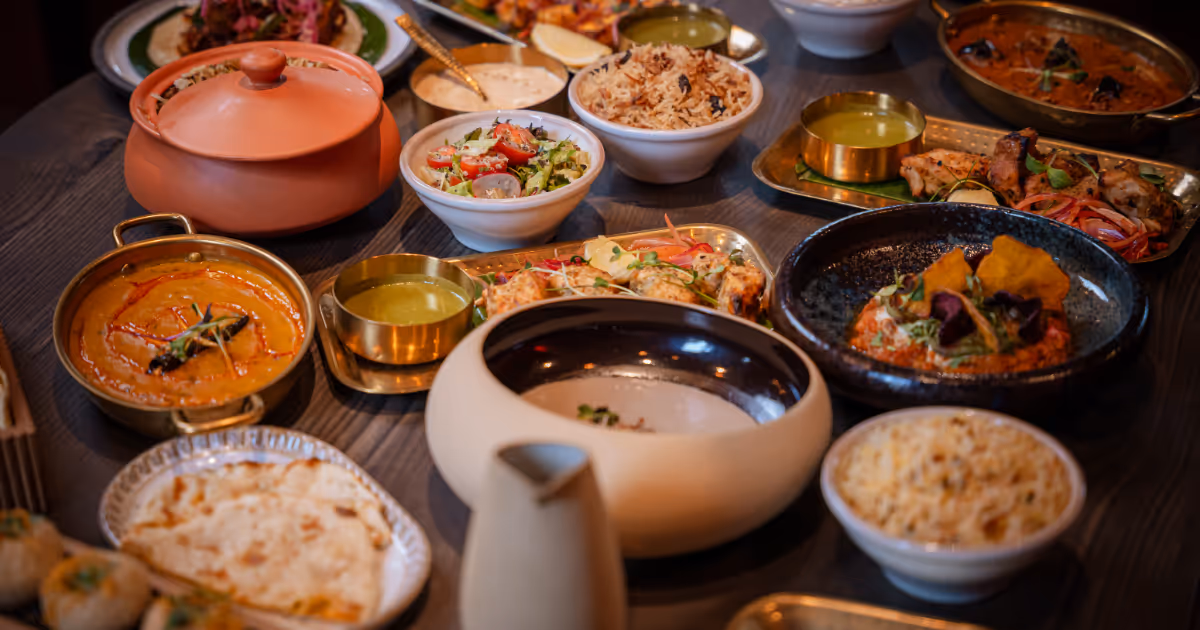 Verschiedene indische Gerichte, darunter Currys, Reis, Salat und Naan, serviert auf einem Holztisch.