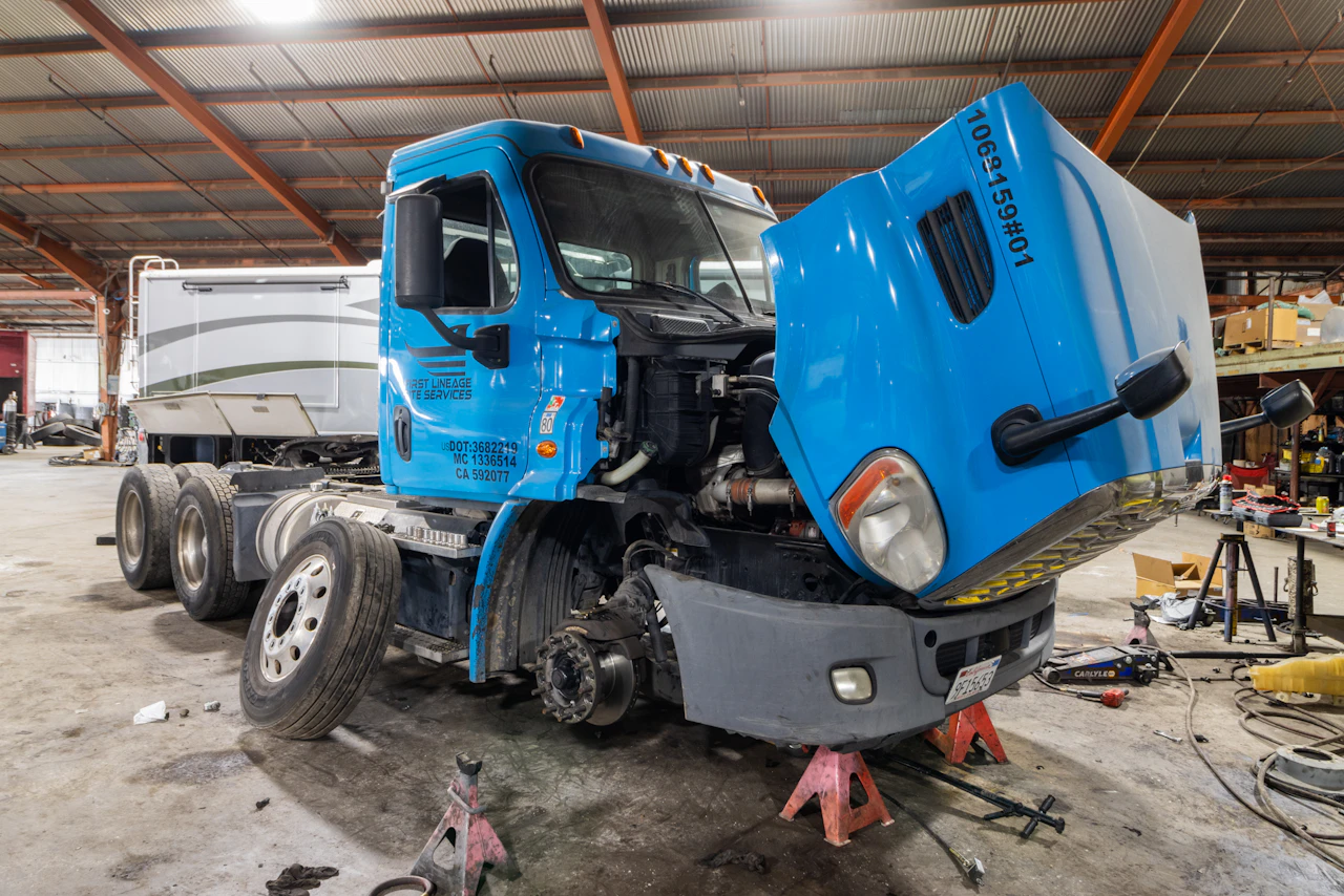 A blue semi truck in repair bay with its hood up. 