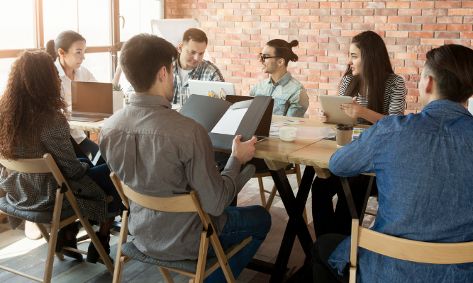 Small business team meeting around a table to plan a marketing strategy on a budget, collaborating on ideas and reviewing documents during a planning session.