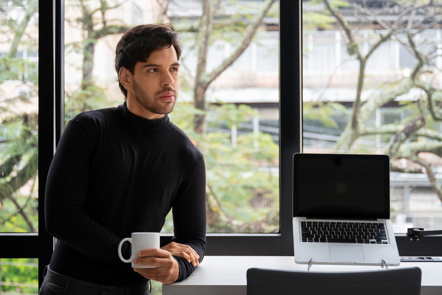 A man in a black shirt sits at a desk, working on a laptop.
