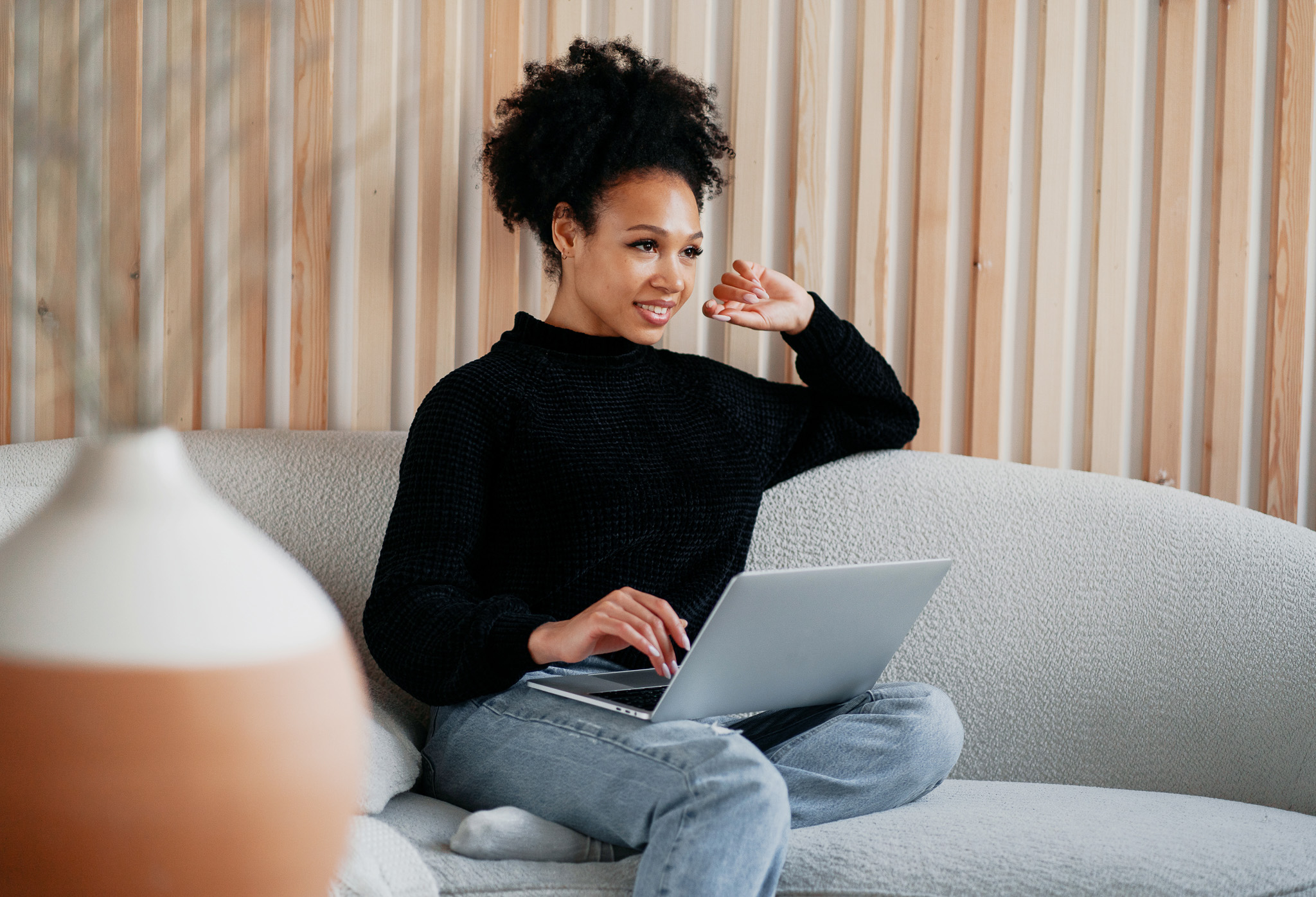 Lady sitting on a couch smiling with laptop.