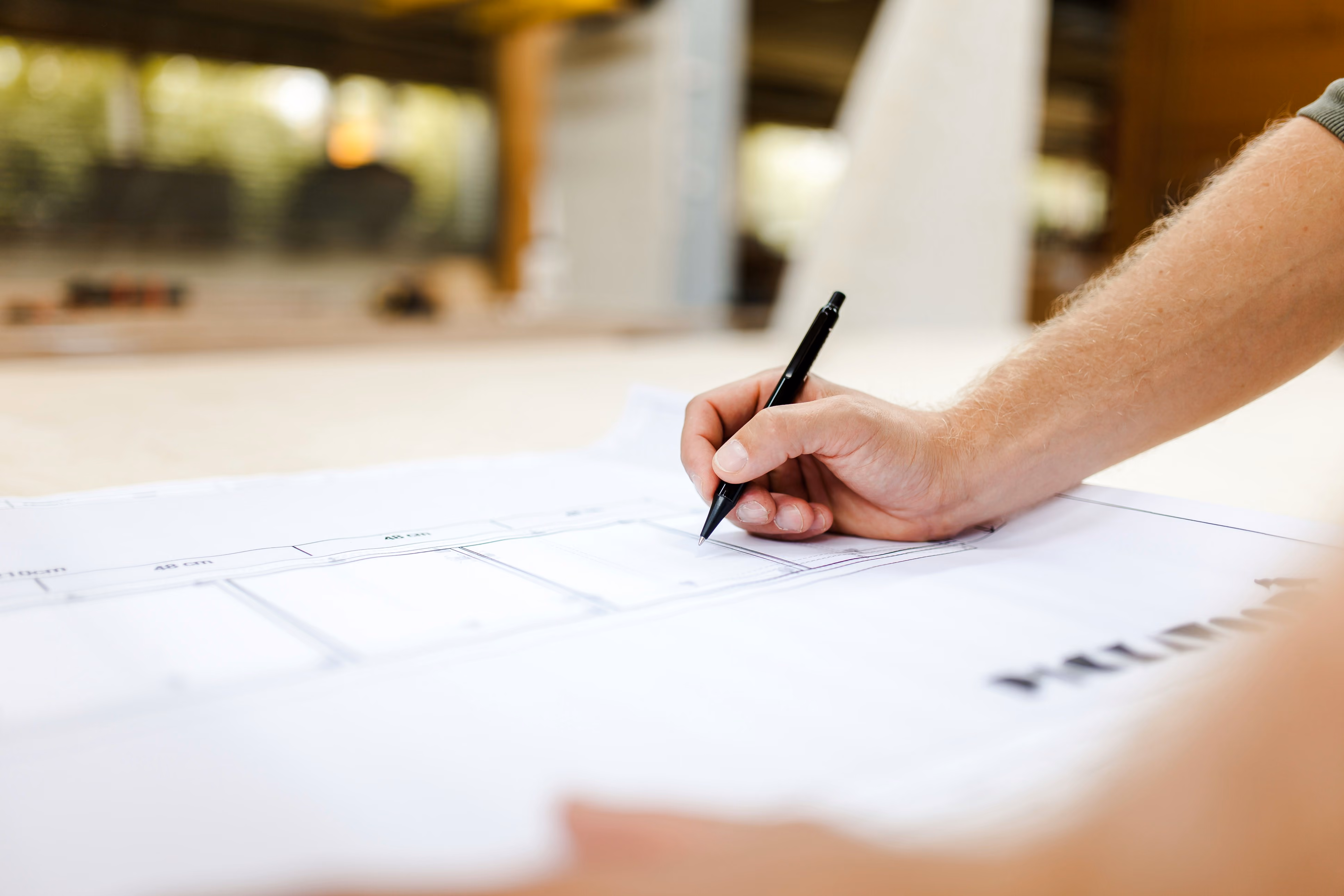 Close-up of a hand marking measurements on a floor plan blueprint with a pen.