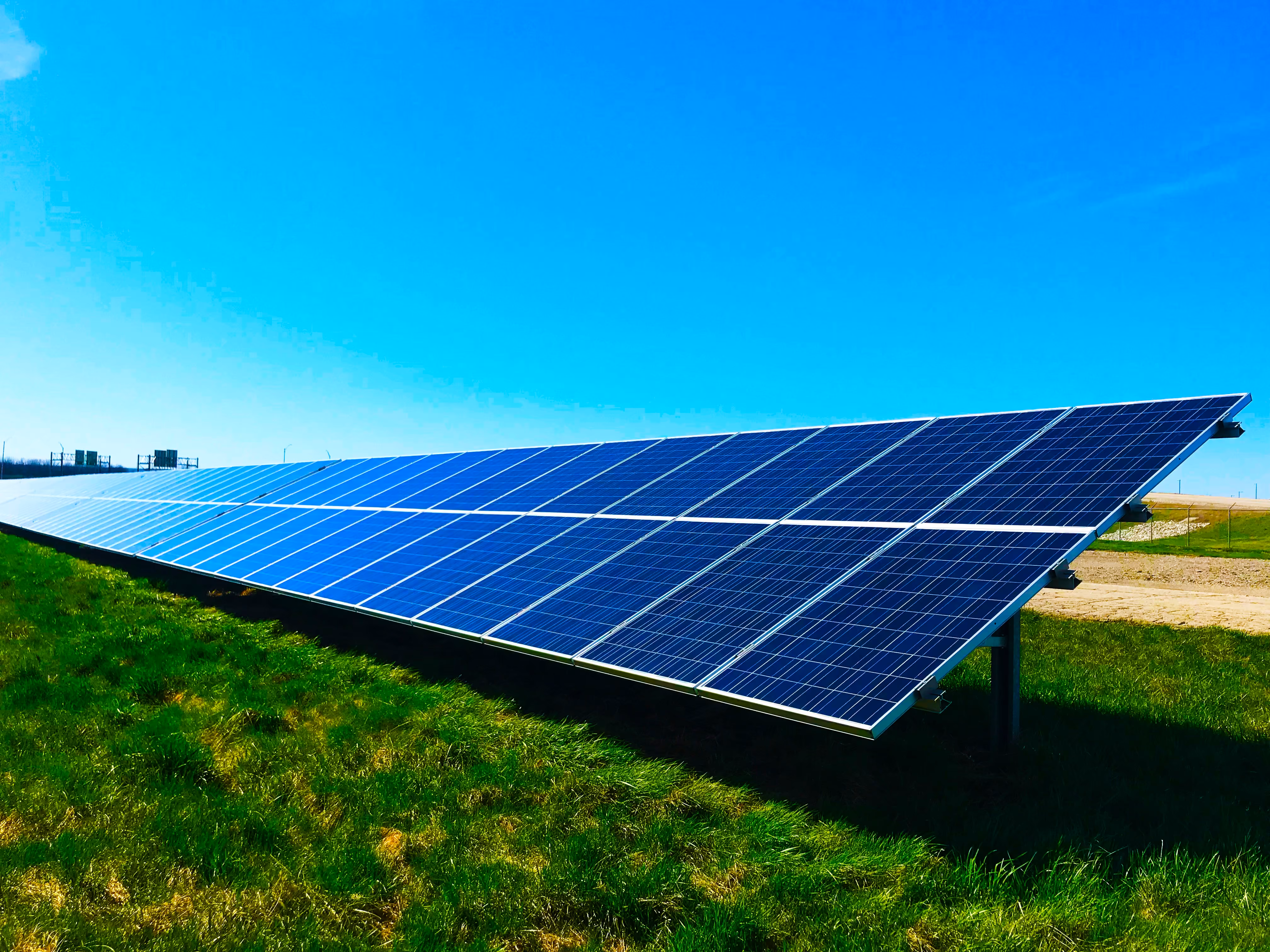 Ground-mounted solar panel array on a grassy field under a clear blue sky.
